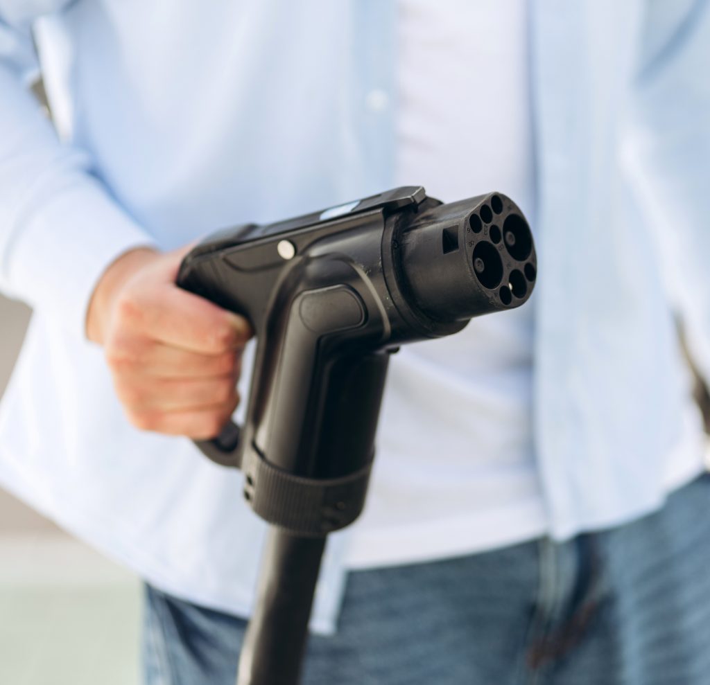Young man holding charging cable at electric charging station point standing near his car. Eco electric car concept