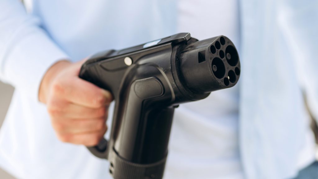Young man holding charging cable at electric charging station point standing near his car. Eco electric car concept